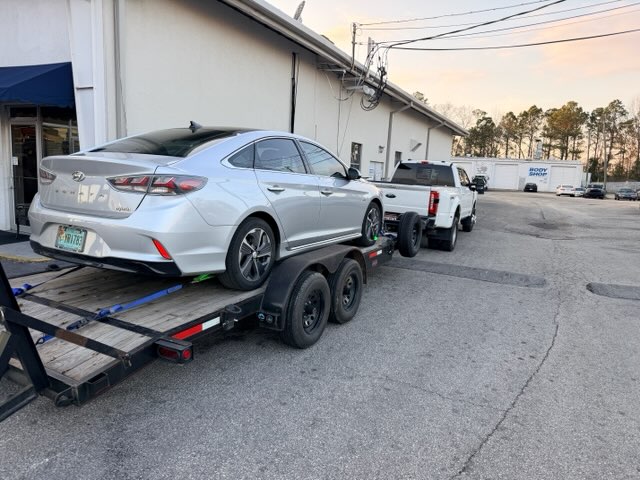 Silver Hyundai Sonata being transported on a flatbed car hauler at dusk